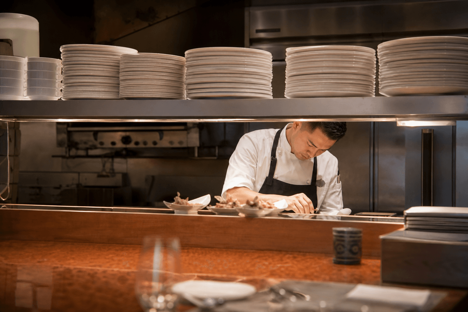 A chef at a Wailea kitchen pass with stacked ivory plates for a full-board retreat day, Pacific through sliders.