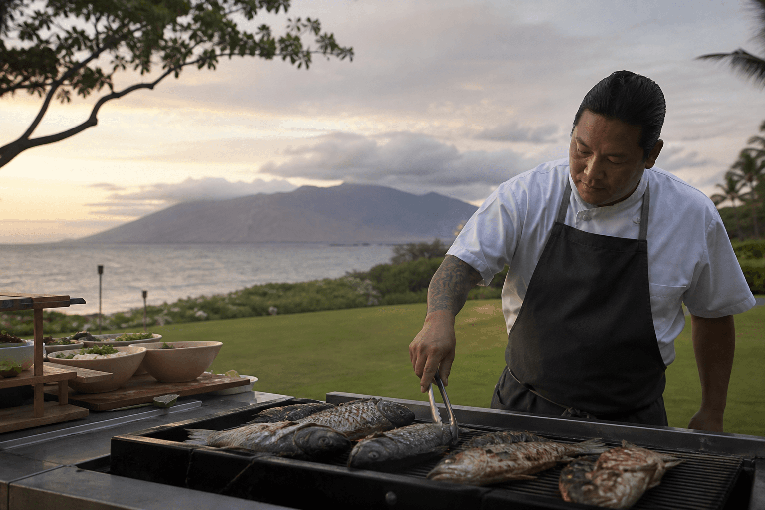 A Wailea lawn grill at dusk — whole fish, grass, Pacific, not a hotel luau.
