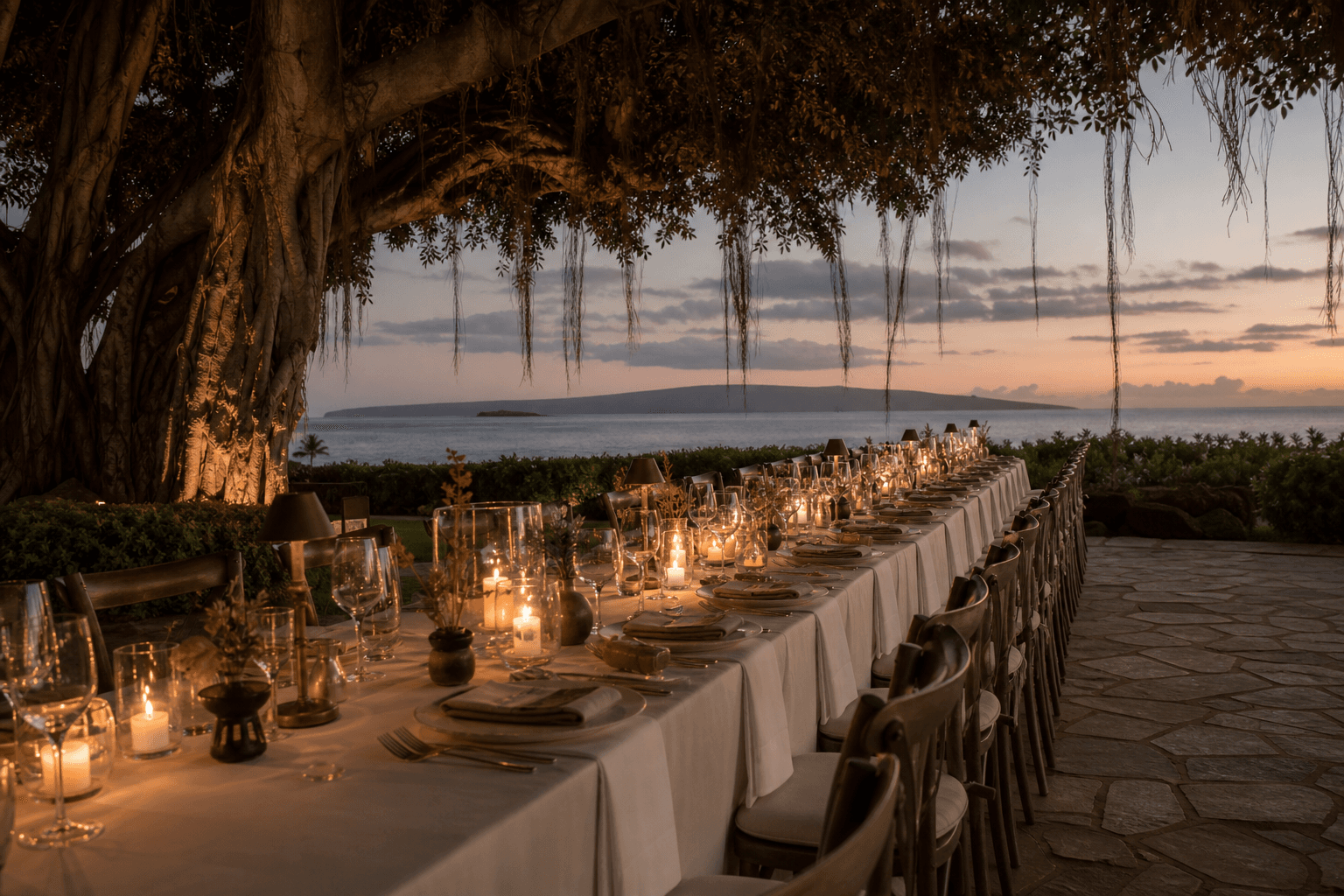 A Wailea wedding-week long table under a banyan at dusk, candles, Pacific beyond.